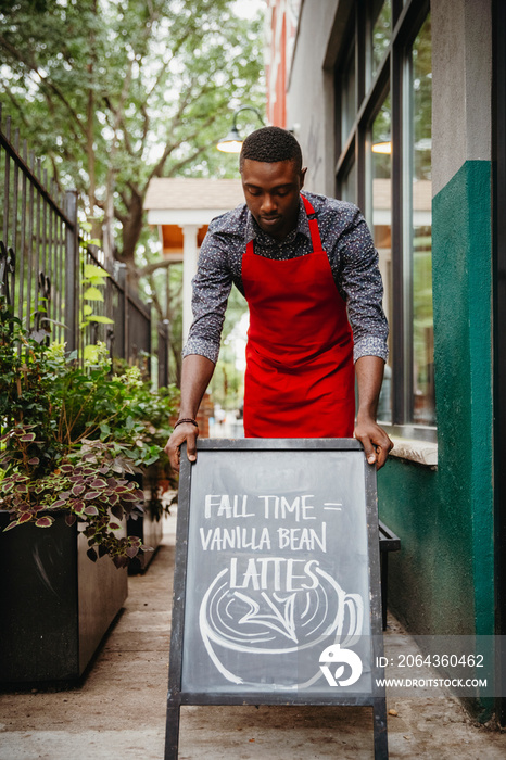 Male manager putting blackboard at cafe entrance