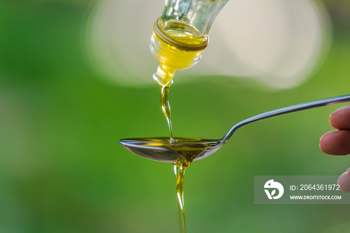 Pouring Olive oil into spoon on Green park garden background