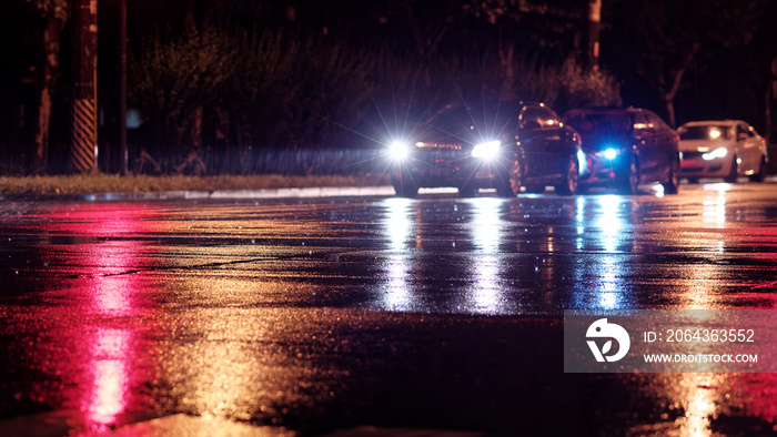 城市的雨夜，由于红色交通灯，汽车在潮湿的道路上等待，雨水被照亮