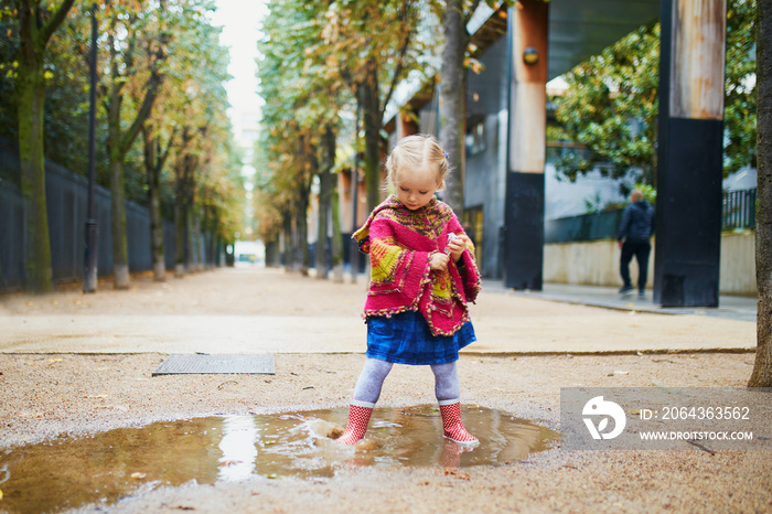 Child wearing red rain boots and jumping in puddle on a fall day