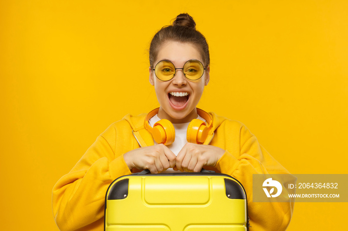 Happy excited teenage girl wearing hoodie, colored glasses and headphones around neck, holding trave