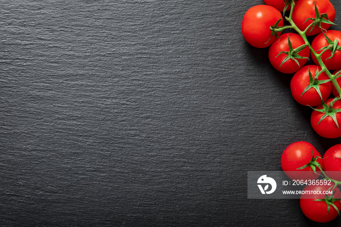 Frische, tiefrote Tomaten am Strang auf schwarzer Schieferplatte als Hintergrund mit Textfreiraum