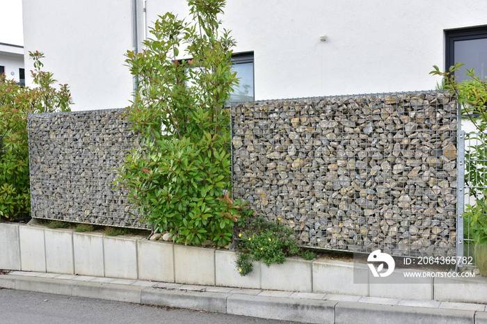 Moderner Sichtschutz- und Lärmschutzzaun aus mit Natursteinbruchstücken gefüllten Gabionen-Stahlgitt