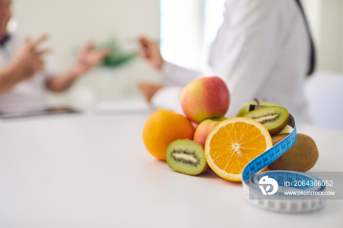 桌子上的新鲜水果和卷尺对着模糊的营养师为患者提供咨询