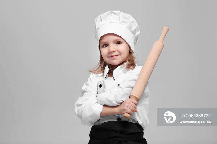 Cute girl in chef uniform on light background