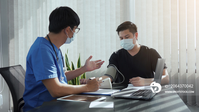 Asian doctor is using a patients blood pressure monitor at the time of his annual check-up and expl