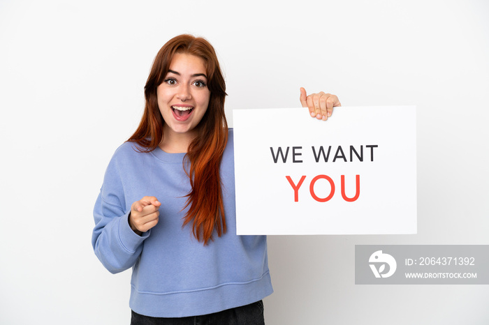 Young redhead woman isolated on white background holding We Want You board and pointing to the front