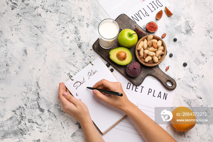 女人在笔记本上写东西，在白色桌子上写健康产品。饮食概念