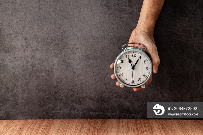 A man holding alarm clock on old gray concrete wall for background.