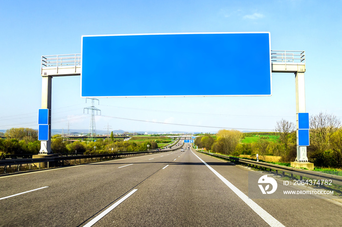 阳光明媚的日子里，路上挂着一块空白的蓝色高速公路标志