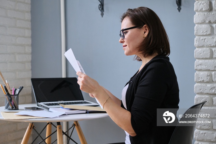 Mature woman sitting at home at desk with laptop, received an envelope with letter