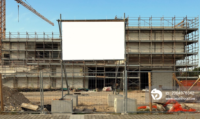 Blank information board near the construction site with a new concrete building among scaffolding