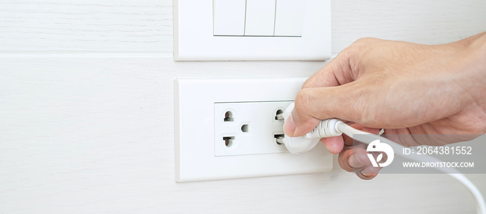 特写男性手指拔下或插入家中白墙上的电力设备。节能