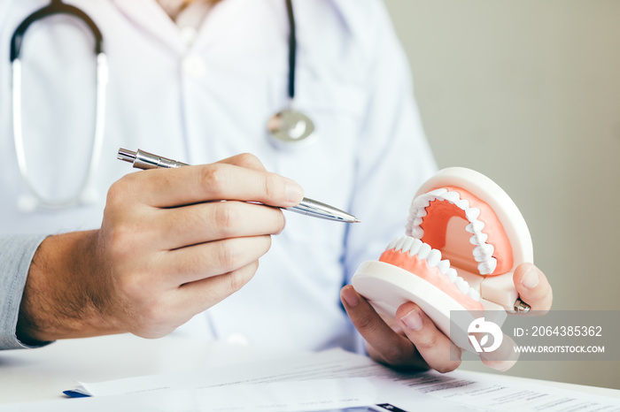 Asian dentist holding pen pointing to the dentures and is describing the problem of teeth.