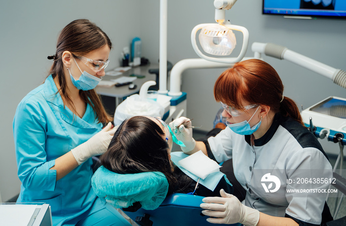 Female dentist and a nurse in masks and protective glasses treating patients teeth. Doctor stomatol