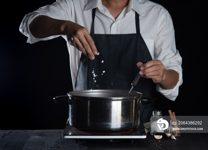 男厨师在黑暗的背景下在锅里放了一些盐，在家做饭