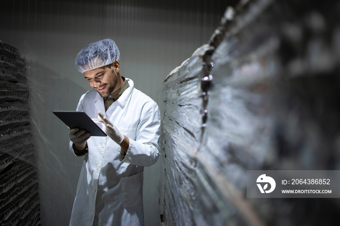 Factory worker with hairnet and hygienic gloves holding tablet computer and checking inventory in fo