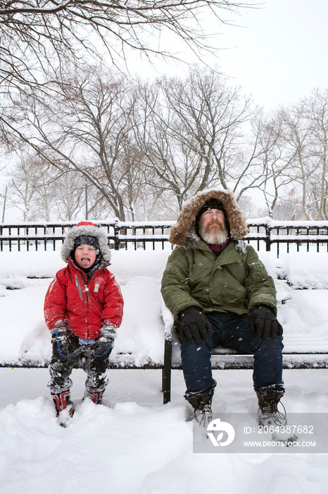 爷爷和孙子在下雪时坐在长椅上