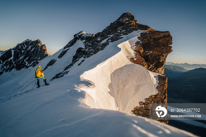 An alpinist climbing a rocky and snow mountain ridge during sunrise. Mountaineering and alpinism in 