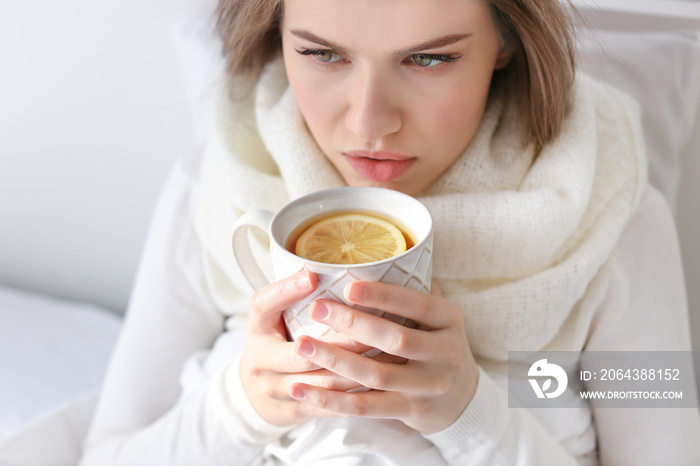 Young ill woman with cup of hot tea in bed at home