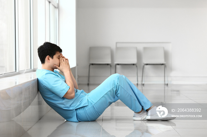 Depressed male medical assistant sitting near window in clinic