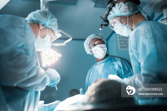 多元文化外科医生在手术室为患者手术的仰视图