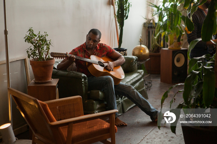 Full length of man playing guitar while sitting on sofa at home