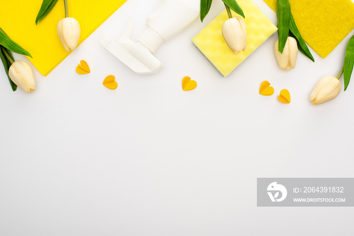 top view of spring tulips and yellow cleaning supplies with hearts on white background