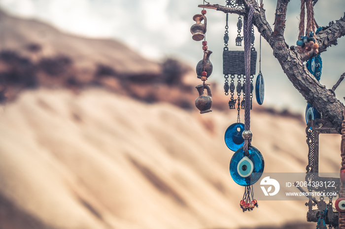 Amulets against evil eye hanging on tree in front of sandy mountain in Cappadocia, Turkey