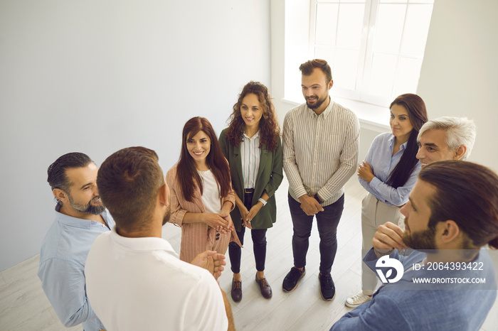 Group of happy young and mature people standing in office and listening to business coach whos shar