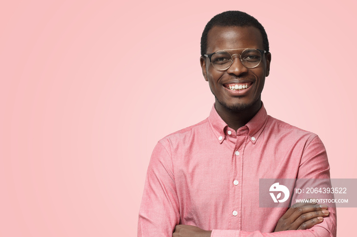 Handsome smiling African American man in formal shirt isolated on pink background standing with cros