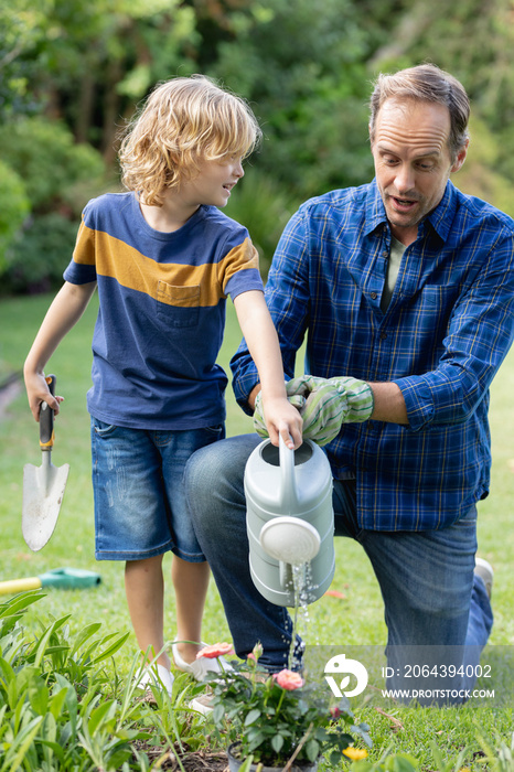 Happy caucasian father in garden with son, watering plants and gardening together