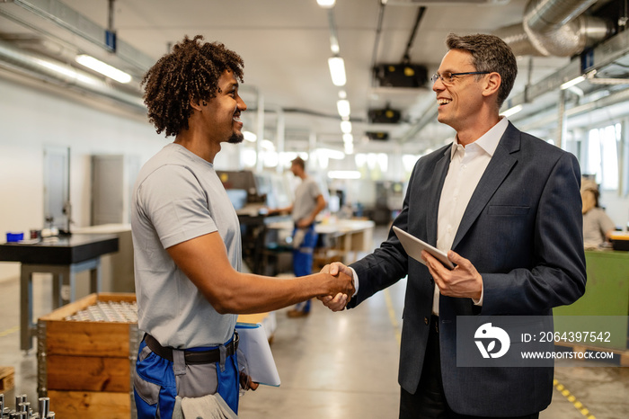 Happy engineer greeting African American worker in industrial building.