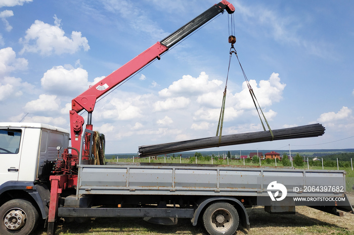 The truck crane in the field on the private land unloads the metal profile.