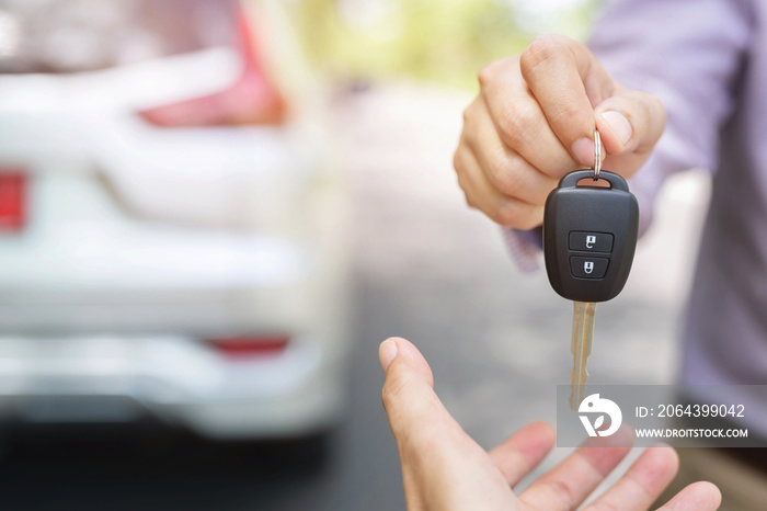 Car key, businessman handing over gives the car key to the other woman on behind the new car backgro