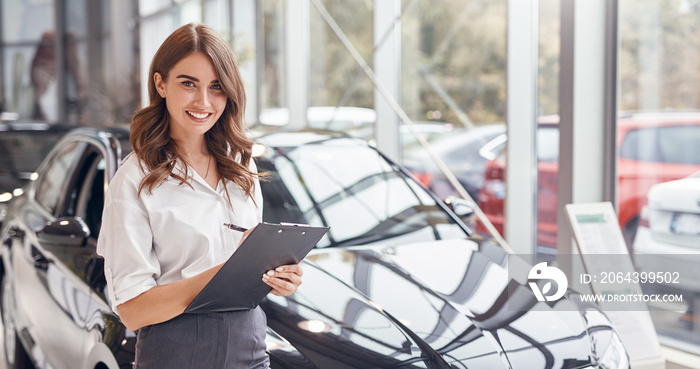 Positive saleswoman with clipboard working in car dealership