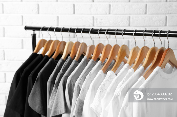 Black, grey and white t-shirts on hangers against brick wall, close up view