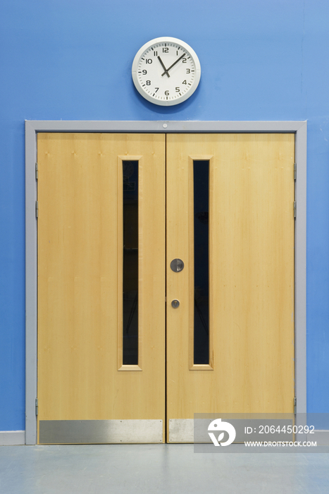 Clock above double doors in the main hall of a secondary school