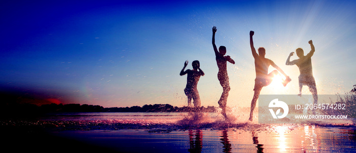 Glückliche junge Menschen laufen und springen am See beim Sonnenuntergang