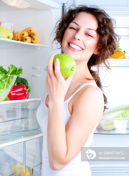漂亮的年轻女人在冰箱旁边，带着健康的食物