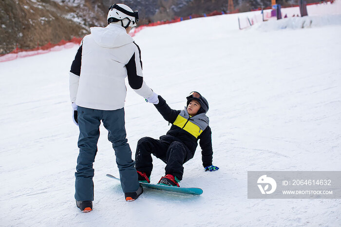 小男孩跟着教练在户外学滑雪