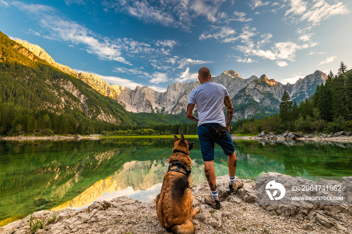 Adventure Man Standing With Dog at Beautiful Lake, Fusine Lake , Italy