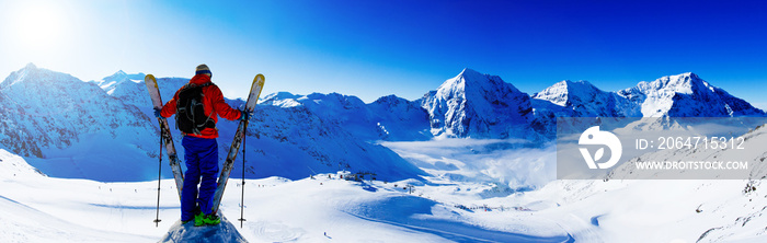 登山者背着滑雪板在雪岭上休息。背景模糊