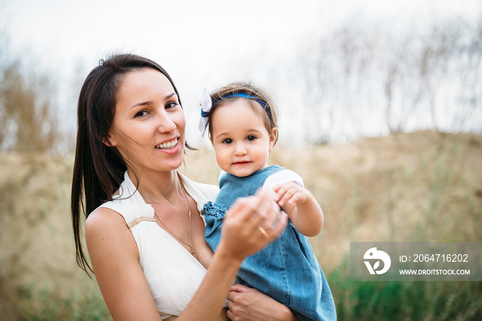 Happy young mother with a small daughter in hands, outdoors background