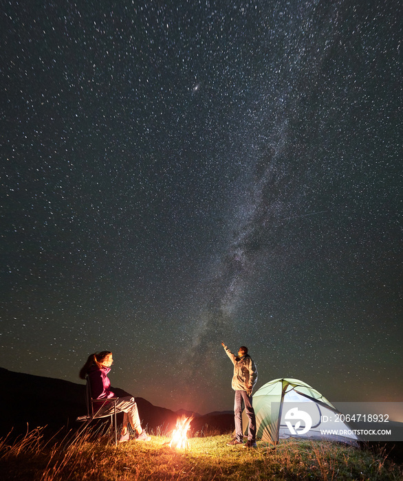 活跃的情侣徒步旅行者在山上享受夏夜露营。坐在b旁边椅子上的女人