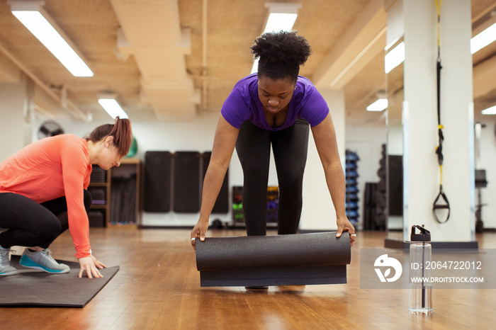 Female athletes placing exercise mats on hardwood floor in yoga class