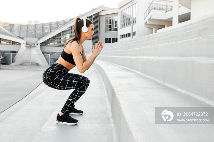 Fit athletic woman exercising doing jumps and squats in outdoor arena stairs