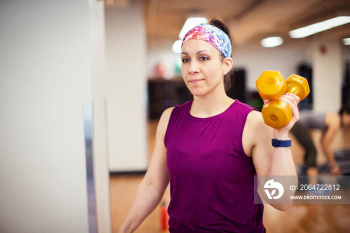 Confident female athlete exercising with dumbbells while standing in gym