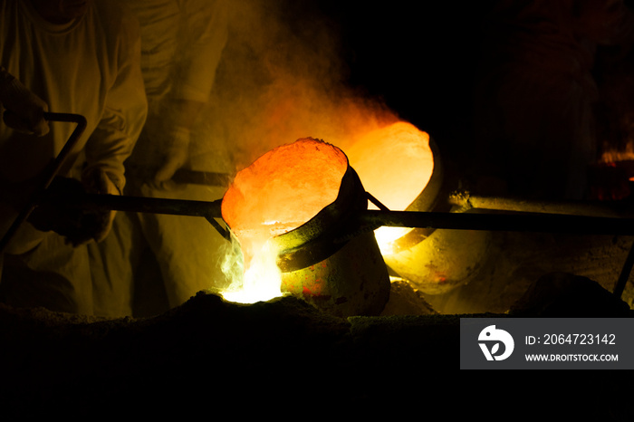 Foundry worker pouring hot molten metal into mold casting