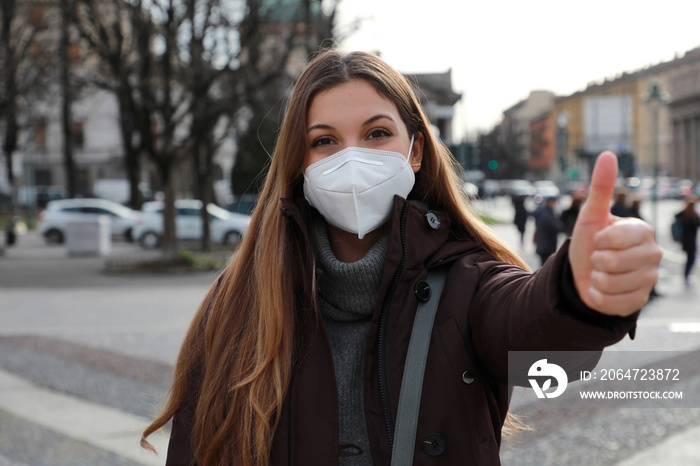 Vaccination campaign. Optimistic young woman wearing protective mask FFP2 KN95 showing thumbs up in 